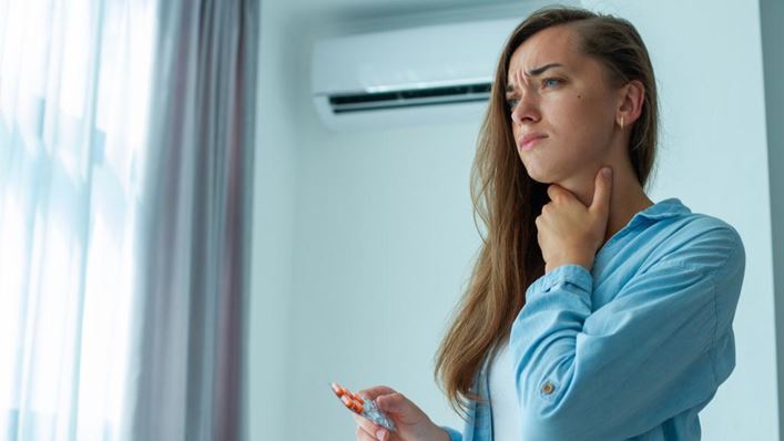 Mujer con dolor de garganta cerca de un aire acondicionado