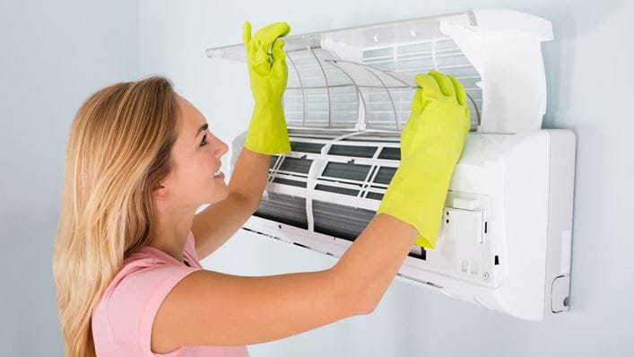 Mujer limpiando la unidad interior del aire acondicionado
