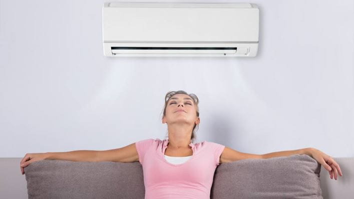 Mujer relajada bajo el aparato de aire acondicionado