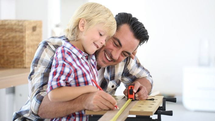 Padre midiendo un listón de madera con su hijo