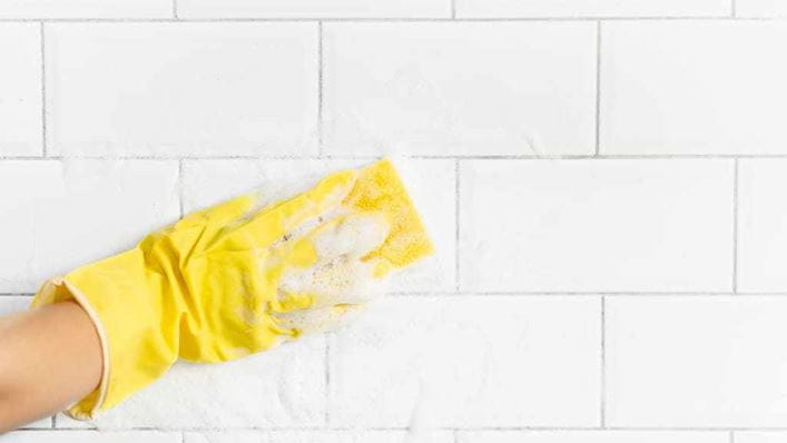 Mano con guantes limpiando los azulejos del baño