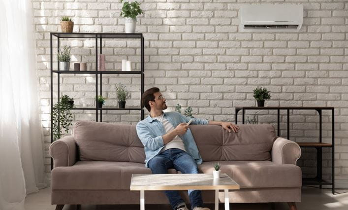 Un chico sentado en el sofá de una habitación con aire acondicionado tipo split en modo DRY