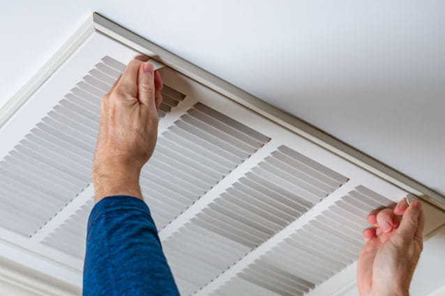 Técnico de aire acondicionado de HomeServe reparando un aire acondicionado por conductos
