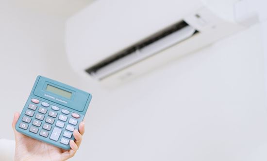 Mano de mujer sujetando una calculadora delante de un aire acondicionado