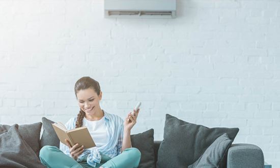 Una chica leyendo en el sofá de una habitación con aire acondicionado