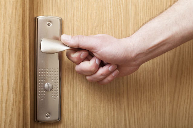 Mano de mujer agarrando la manilla de una puerta de madera