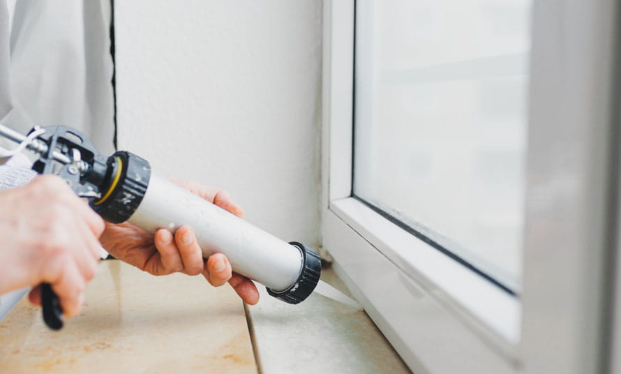 Un hombre haciendo tareas de bricolaje con silicona en la ventana de una casa