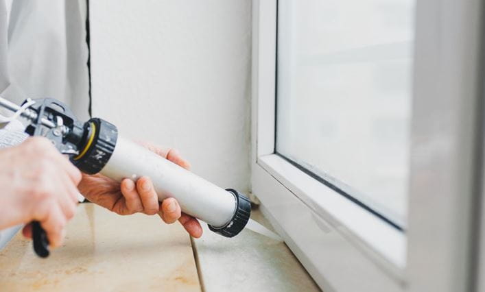 Un hombre haciendo tareas de bricolaje con silicona en la ventana de una casa