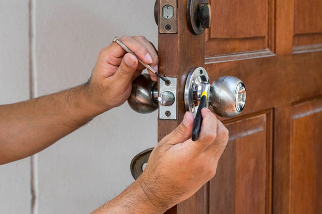 Manos de hombre arreglando la cerradura de una puerta de madera