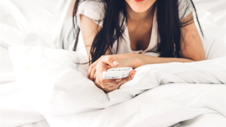 Mujer encendiendo el aire acondicionado desde la cama