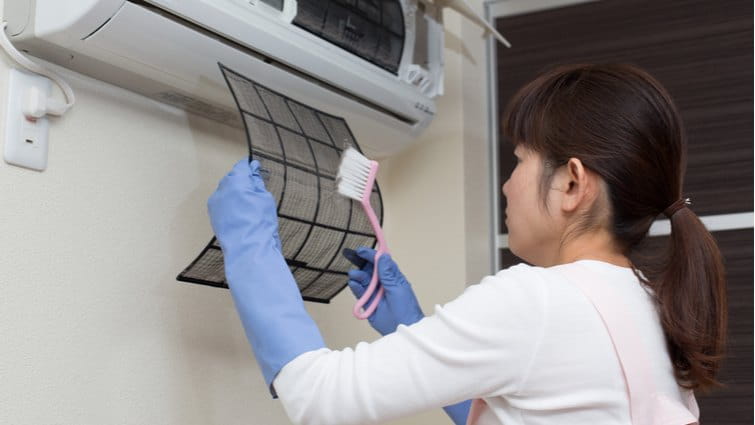 Mujer limpiando los filtros del aire acondicionado con un cepillo