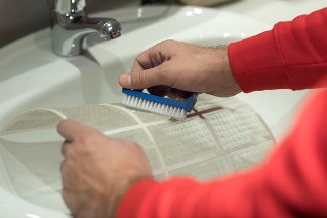 Técnico de HomeServe limpiando los filtros de un aire acondicionado con agua y jabón