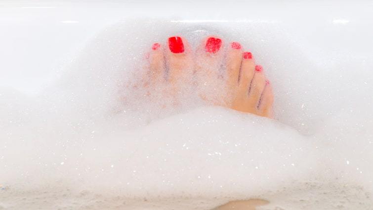 Pies de mujer con uñas rojas disfrutando de un baño con espuma