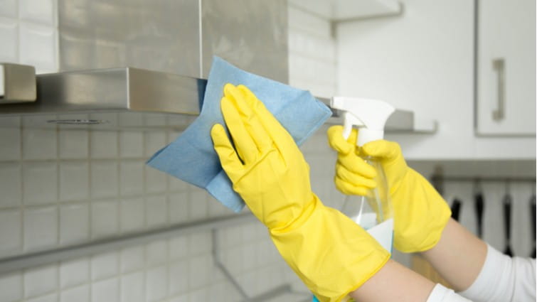 Mujer con guantes limpiando el exterior de una campana extractora