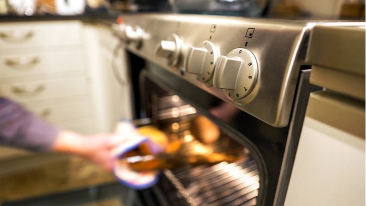 Persona sacando una bandeja del horno con los mandos en primer plano