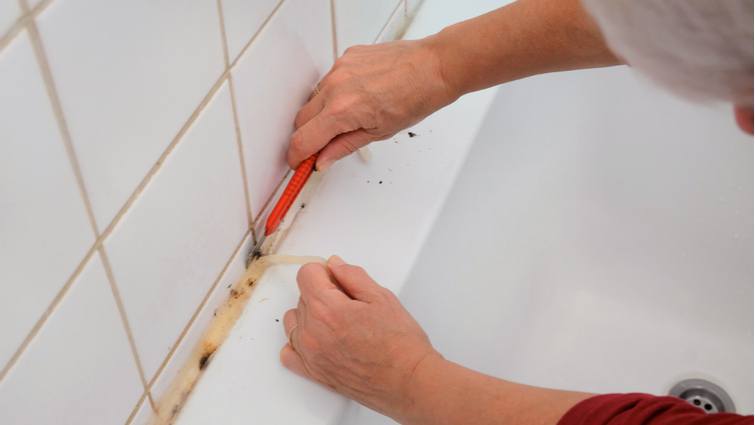 Manos de hombre retirando la silicona de la bañera con un cúter