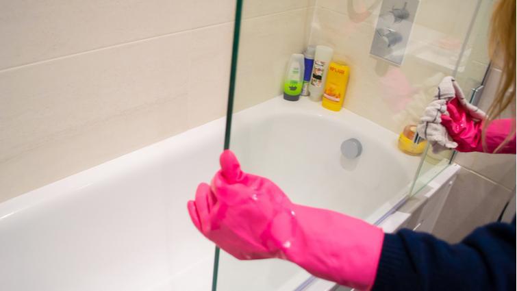 Mujer con guantes limpiando una mampara con un trapo