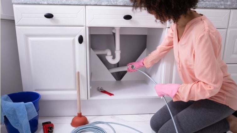 Mujer utilizando un desatascador de muelle en el lavabo