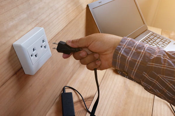 Mano de un hombre conectando un ordenador en un enchufe de pared sin empotrar