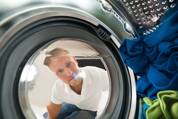 un chico mira en el interior de una lavadora que hace ruido al centrifugar