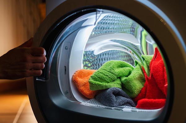 Mano de hombre sacando la ropa del interior de una secadora que no calienta