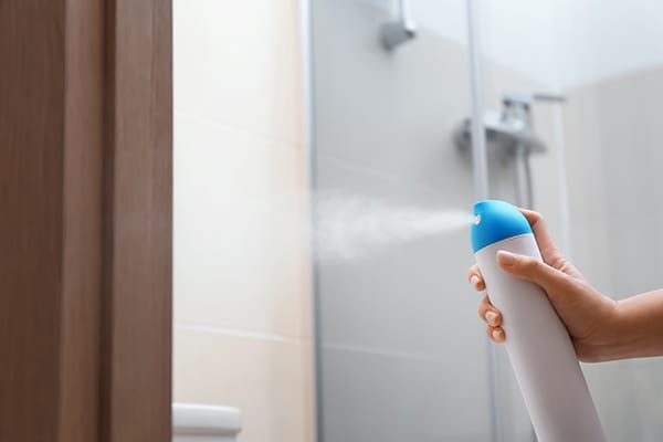 Mujer rociando ambientador en un baño con mal olor