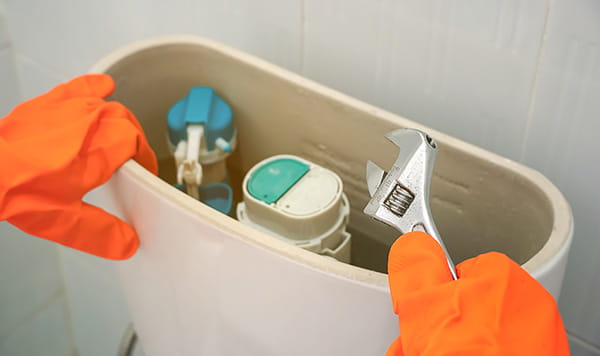 Manos de mujer con guantes naranjas reparando una cisterna roca