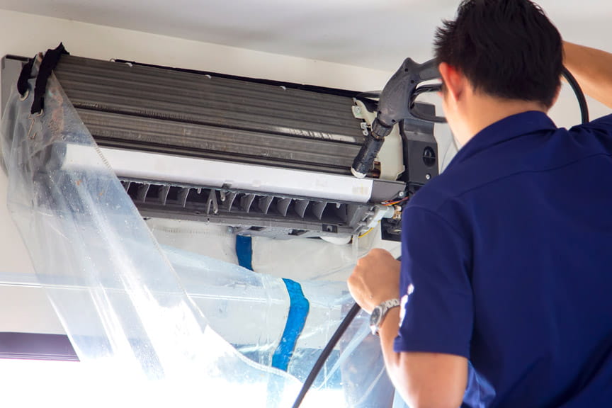 Técnico de aire acondicionado de HomeServe reparando en casa de unos clientes un aire acondicionado negro